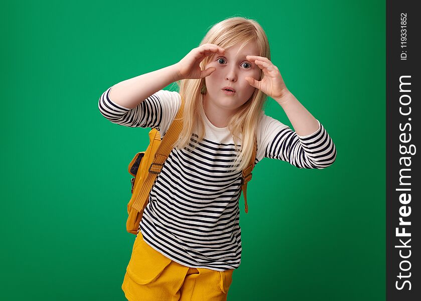 Surprised school girl with backpack looking through binocular shaped hands on green background. Surprised school girl with backpack looking through binocular shaped hands on green background