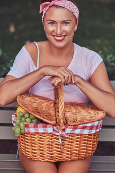 Happy Beautiful Redhead Female Wearing Casual Clothes Holds A Picnic Basket While Sitting On A Bench In A Park. Royalty Free Stock Images