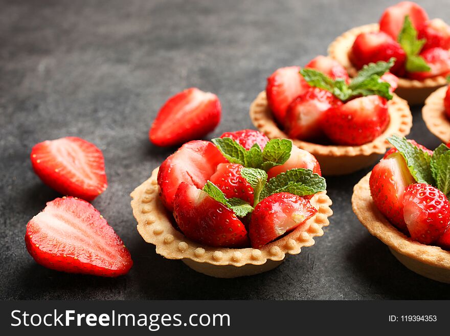 Tartlets with ripe strawberries and mint on a black background.
