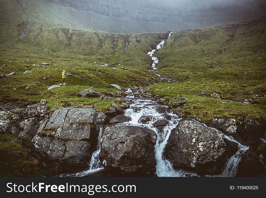 Man with yellow raincoat looking waterfall in faroe