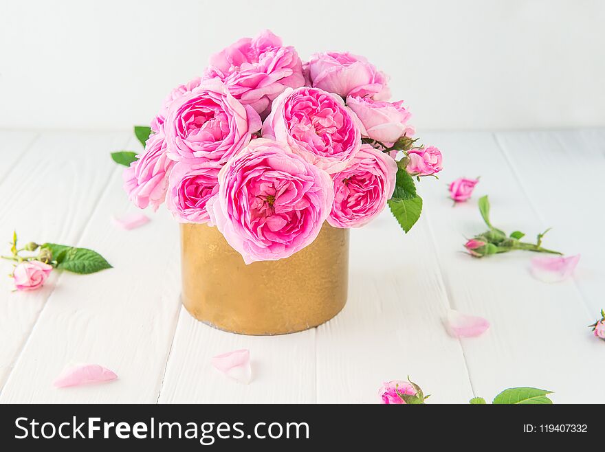 Close up tender pink tea roses bouquet in vintage golden pot on the white wooden table. Floral background. Postcard mock up. Summer, spring flowers. Selective focus. Copy space