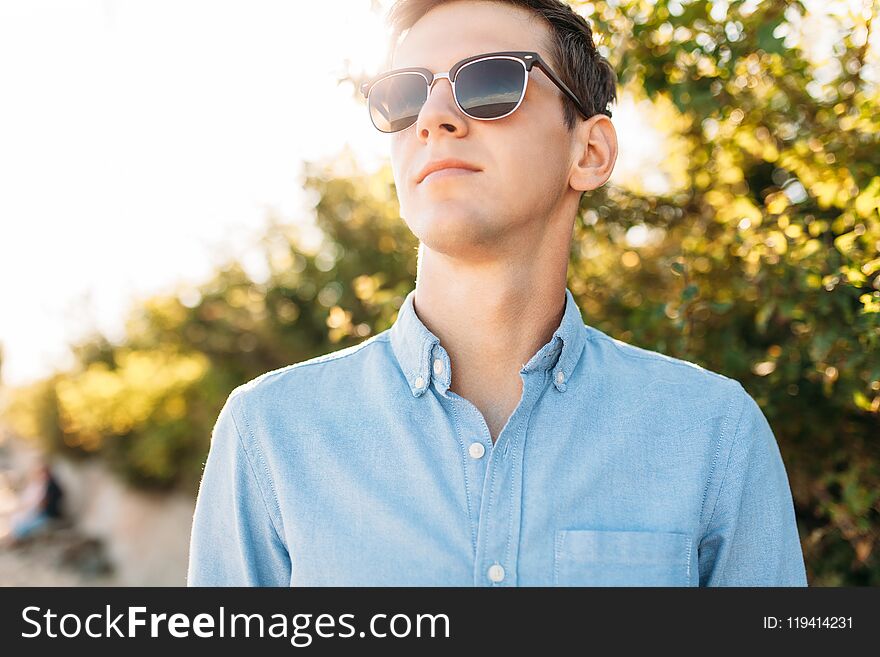 Beautiful stylish guy with glasses, posing on the beach, at sunset, hipster posing in stylish clothes, for advertising, text inser