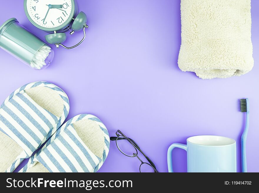 Home equipment clock flat lay composition tooth brush glasses, towel and slippers top view on blue and purple violet concept