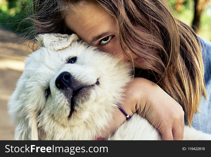 Happy teen girl embracing a cute puppy of a pyrenean mountain dog holding it on her hands in summer day outdoors