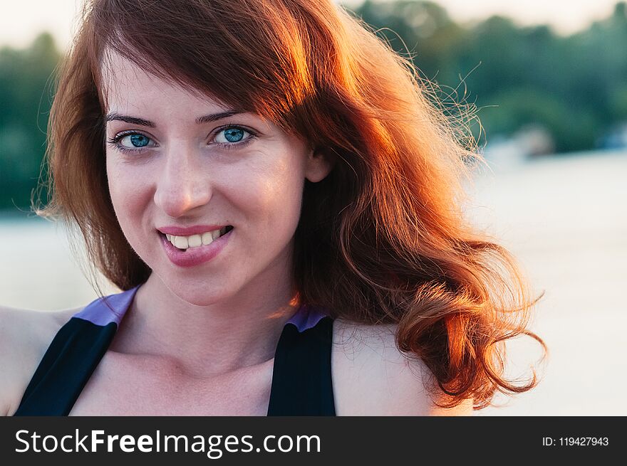 Close up portrait of a young beautiful ginger haired woman, biting her lip in a smile, white teeth, looking at camera, on water summer nature background. Close up portrait of a young beautiful ginger haired woman, biting her lip in a smile, white teeth, looking at camera, on water summer nature background