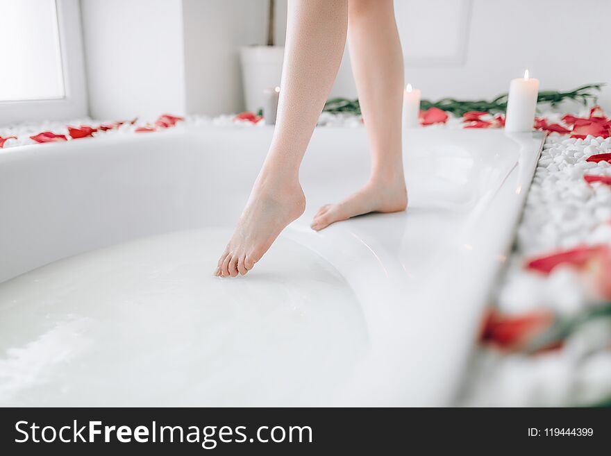 Woman in white bathrobe dips legs into the bath