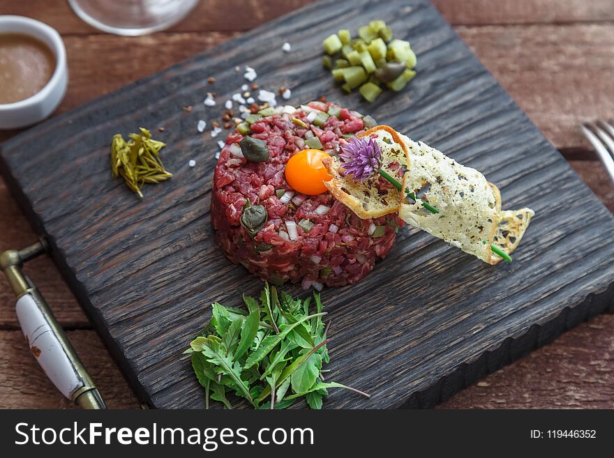 Beef tartare with capers, pickled cucumber and fresh onions on dark background