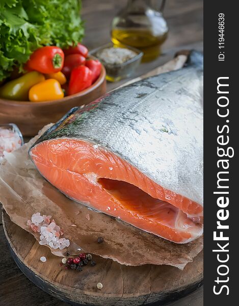 A large piece of salmon lies on a wooden table for cooking. Horizontal frame.