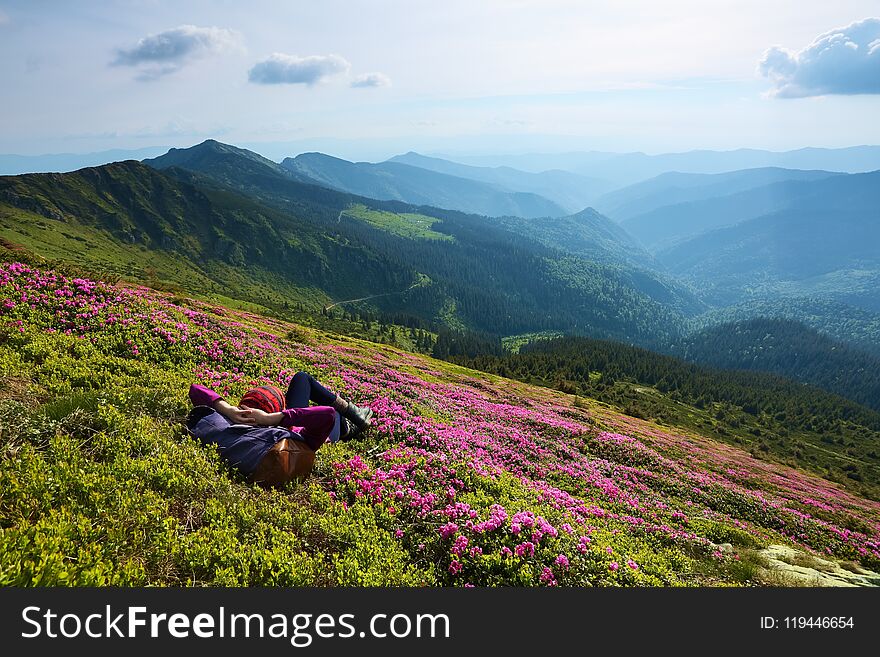 The landscape with the high mountains. Sky with clouds. Forest road. On the lawn of the rhododendrons the girl is laying.