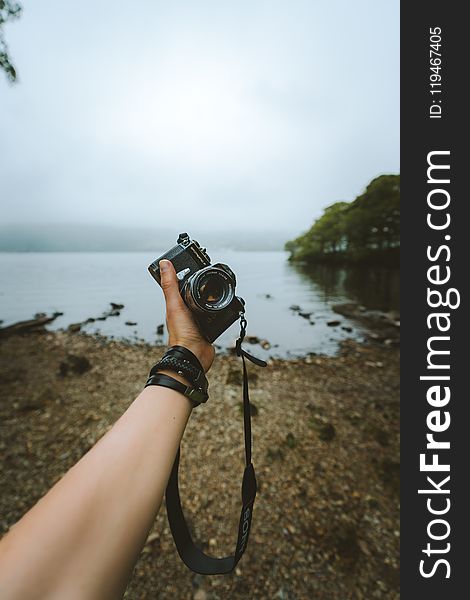 Person Holding Black Camera Front Body Of Water