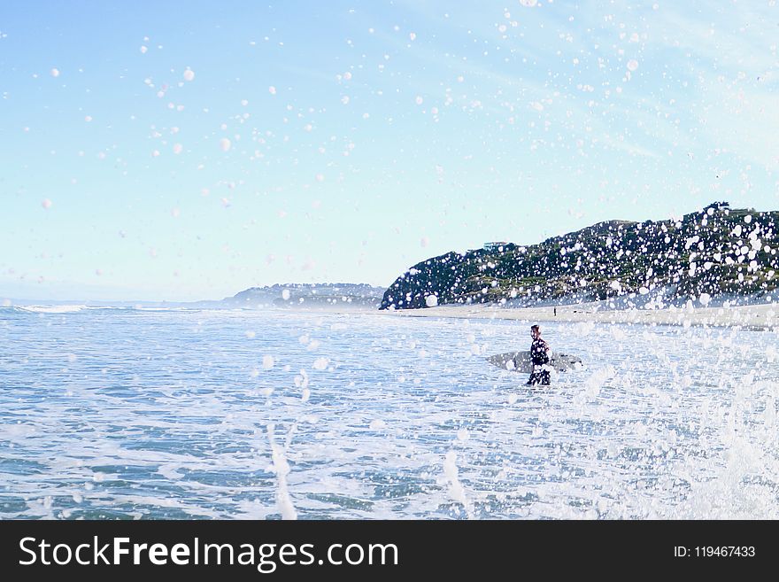 Person Carrying Surfboard Walking on Sea Water