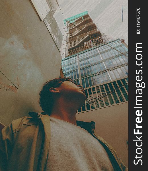 Man in Brown Jacket Looking up at a Tall Building
