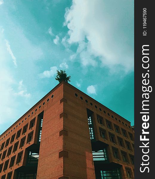 Brown Concrete Building Under Teal and White Cloudy Sky at Daytime