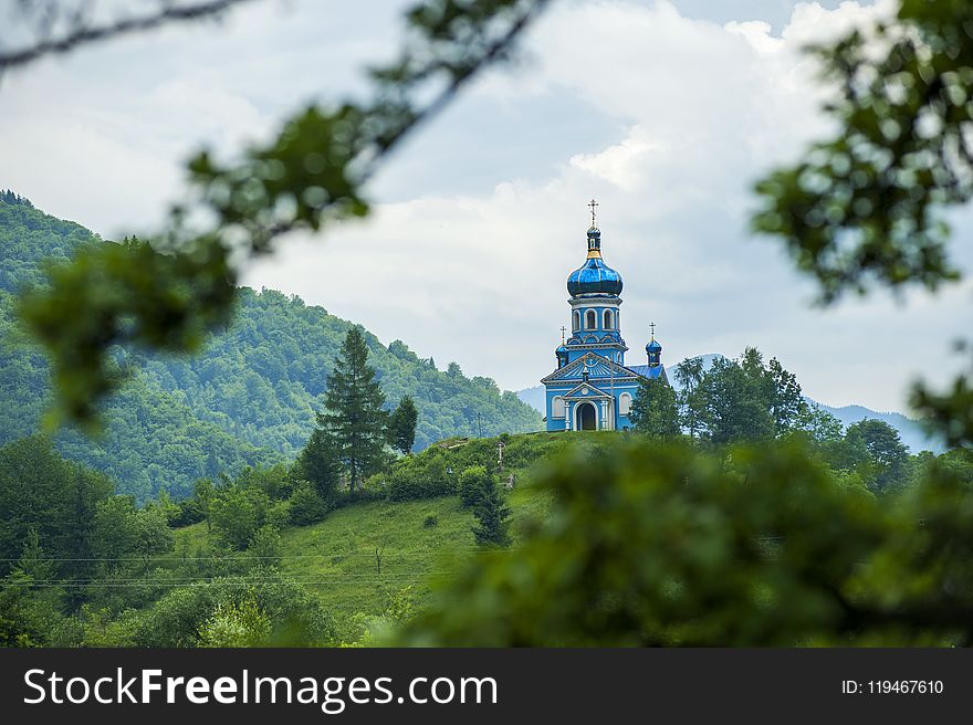 Blue Dome Building Surrounded by Tall Trees Taken Under White Clouds