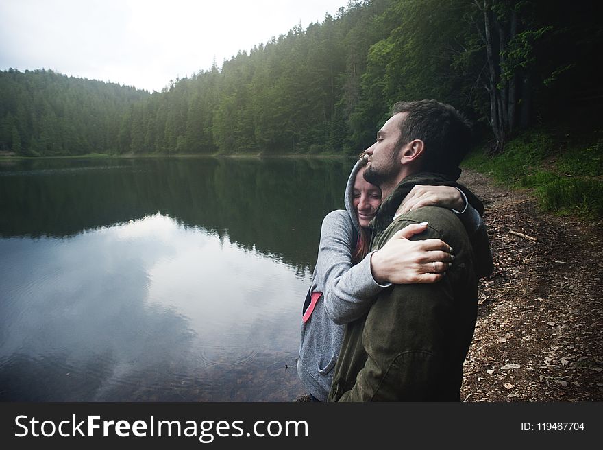 Woman Hugging Man Standing Beside Body of Water