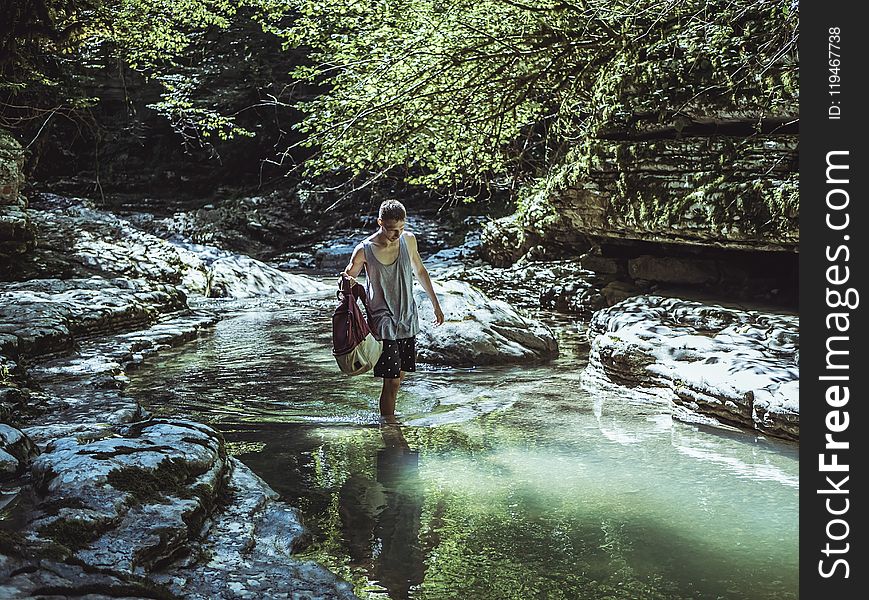 Man Walking On River In Between Stone And Tree