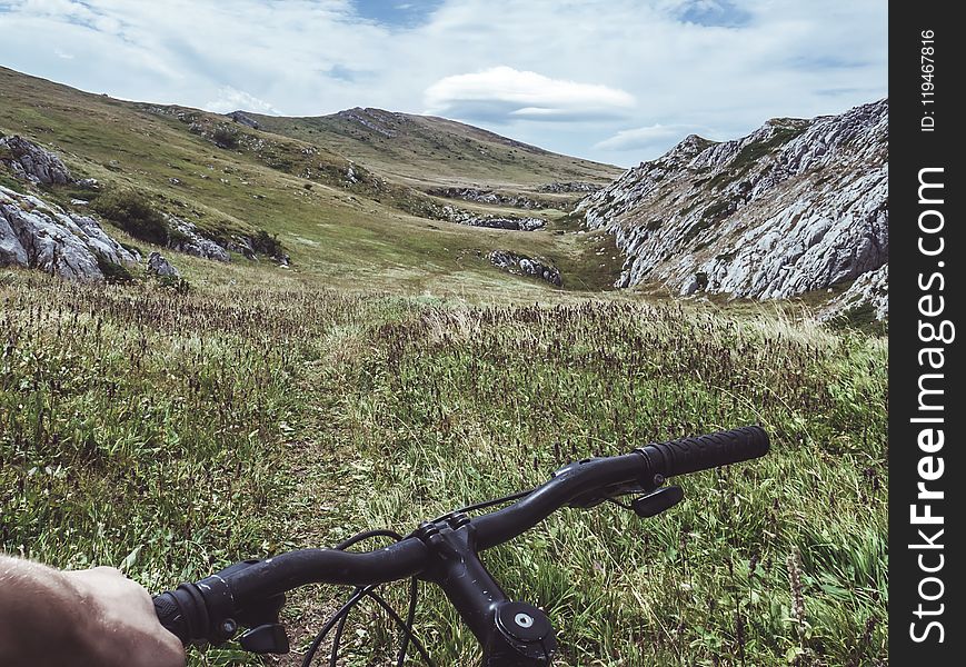 Person Riding Bicycle Overlooking Green Grass Field and Hill