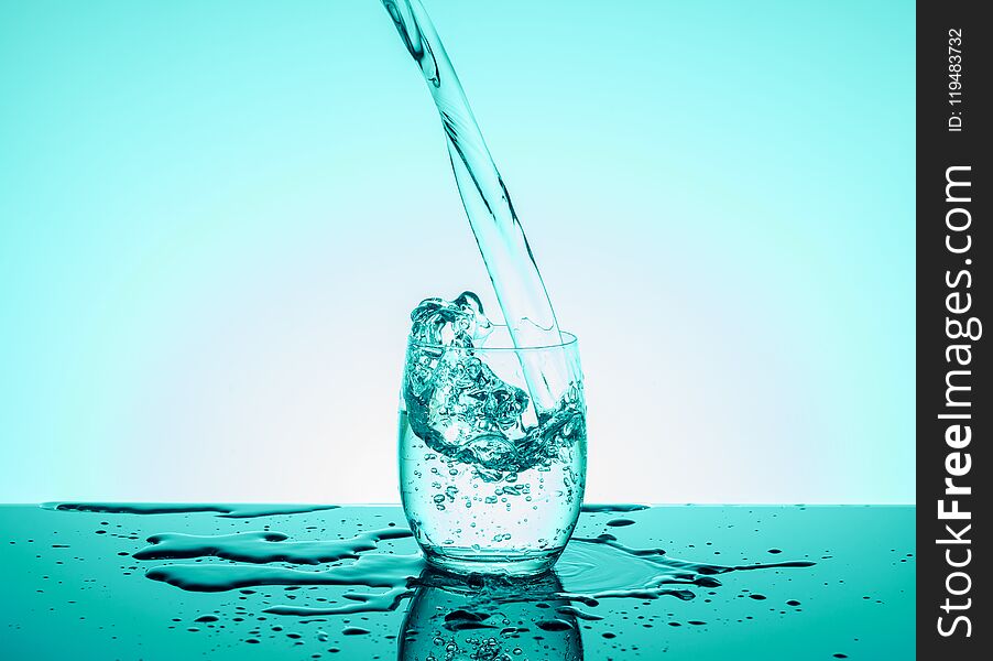 Creative splashing water in the glass on blue background.