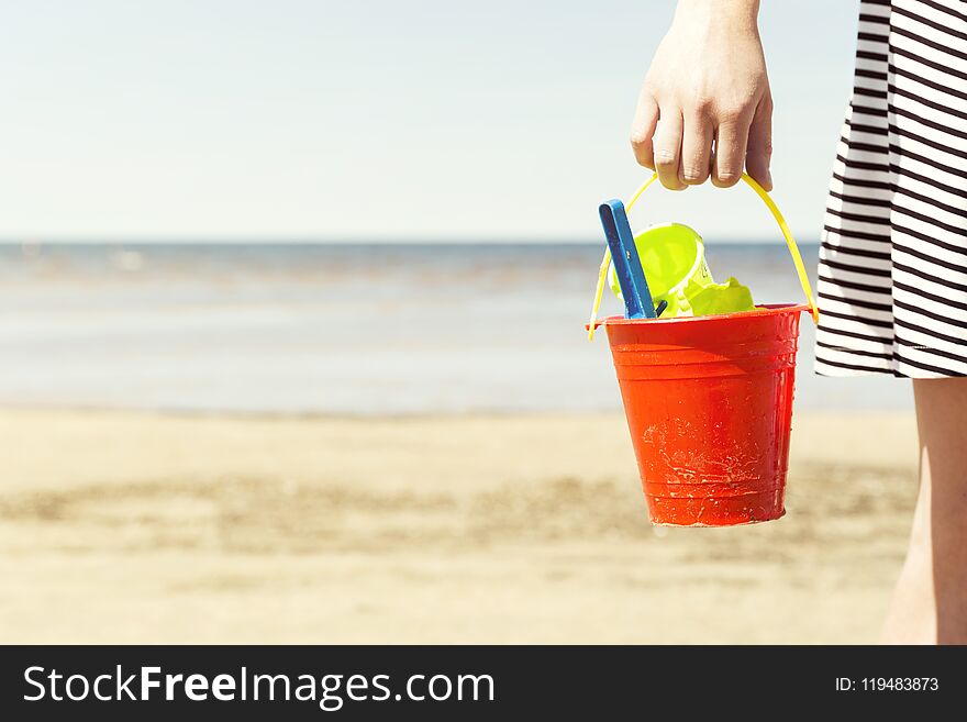 Woman holding bucket with children`s beach toys - spade and shovel on a sunny day