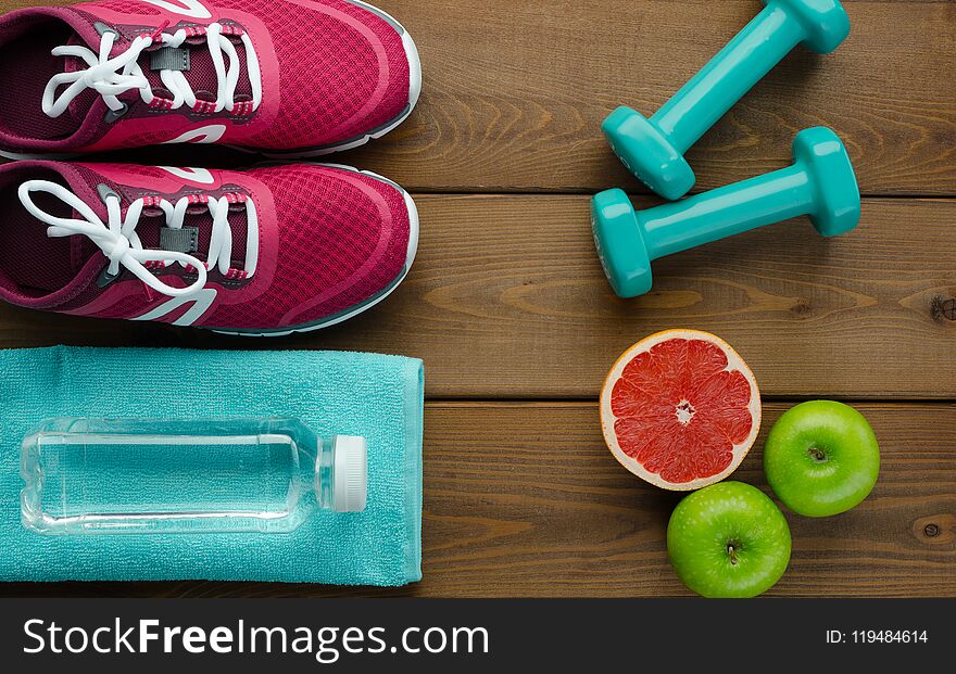 Fitness concept with sneakers dumbbells bottle of water apple pomelo and measure tape on wooden table background