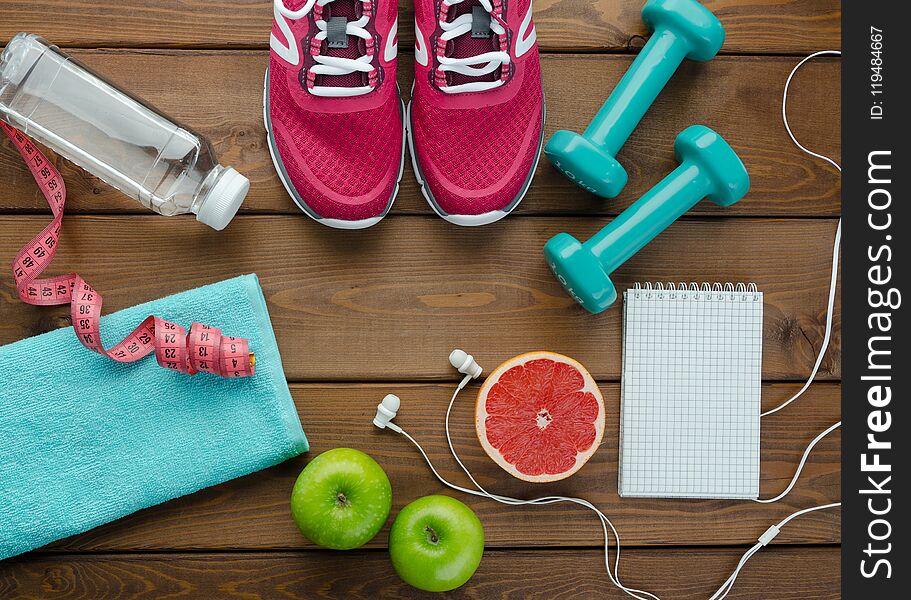 Fitness concept with sneakers dumbbells bottle of water apple pomelo and measure tape on wooden table background