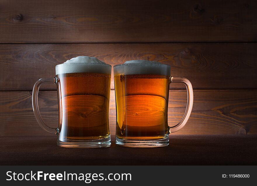 Two glasses of golden beer on wooden background