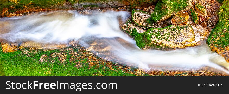 Water cascade of small creek between mossy stones. Long exposure.