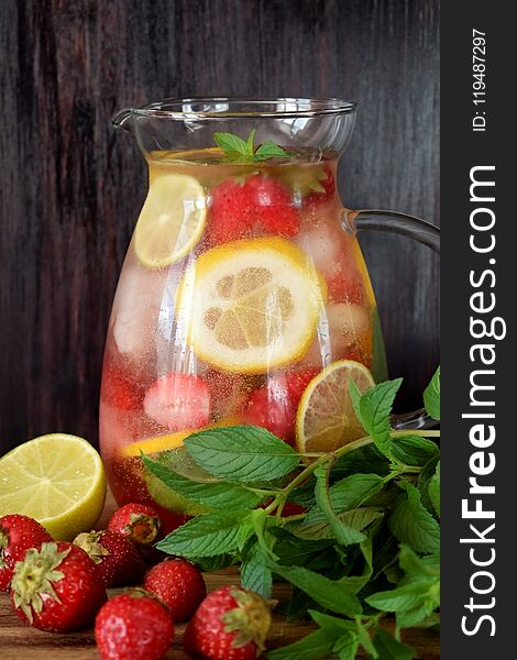 Lemonade with strawberry, lemon, mint, lime and ice cubes in a glass jug surrounded by the ingredients