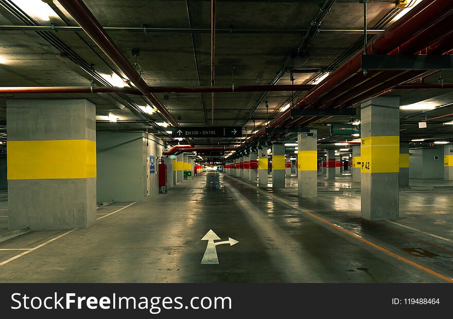 Perspective view of empty indoor car parking lot at the mall. Underground concrete parking garage with open lamp at night.