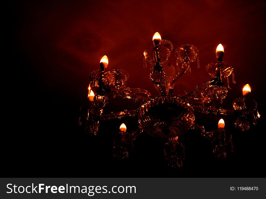 Luxury glass chandelier mounted on ceilings of the room. Red warm light from chandelier reflection on the wall