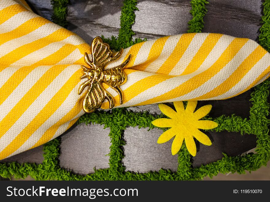 Yellow and white crisp linen napkin with gold bee napkin ring on a placemat that looks like paving stones with grass- springtime t