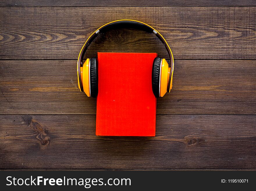 Audiobooks Concept. Headphones Put Over Hardback Book With Empty Cover On Dark Wooden Background Top View Copy Space