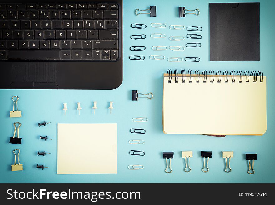 On a blue background there is an open notepad on the springs. Staples, buttons and paper clips are neatly arranged in rows. Beautiful pattern, mock up. Photo with a vignette.