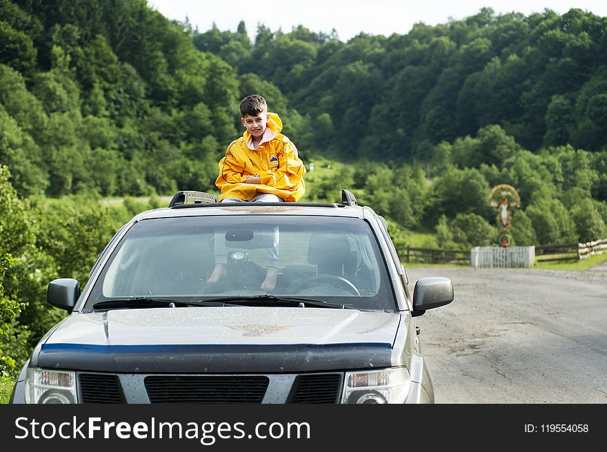 Child in Yellow Jacket Sitting on Roof of Nissan Frontier Through the Sunroof