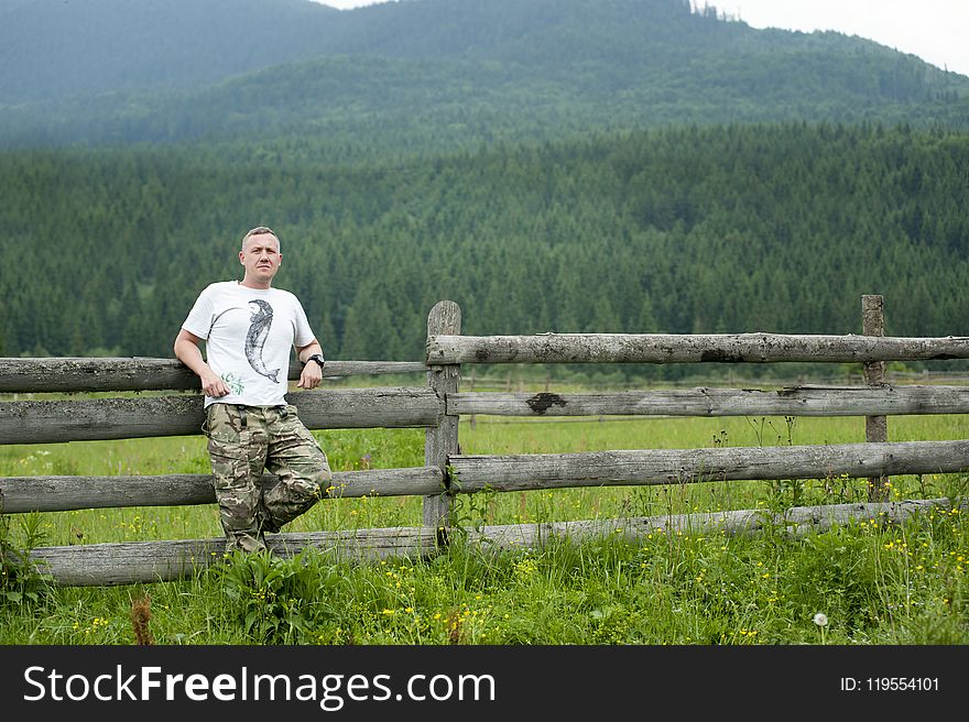 Photo of Man Leaning on Wooden Fence