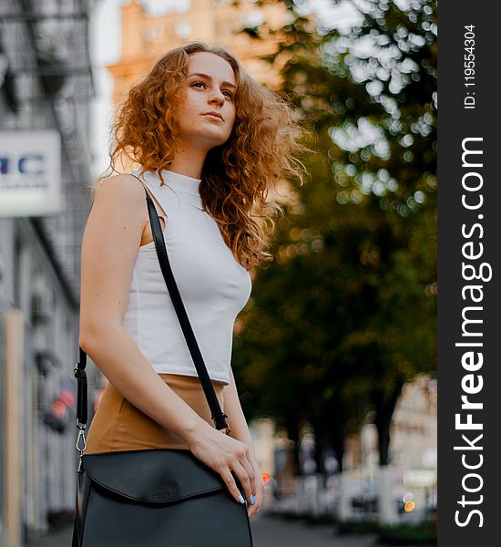 Woman in White Turtleneck Sleeveless Top and Brown Bottoms Holding Black Leather Crossbody Bag Outfit