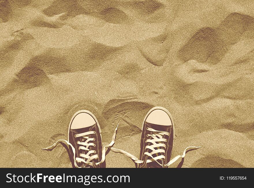 Looking down on pair of blue unlaced sneakers standing side by side on beach sand. Hot sunny weather. Summer vacation. Retro styled photo. Copy space. Looking down on pair of blue unlaced sneakers standing side by side on beach sand. Hot sunny weather. Summer vacation. Retro styled photo. Copy space