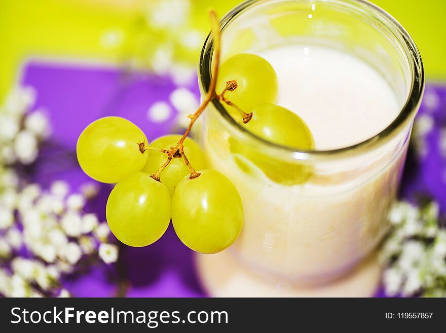 Green grapes on glass with buttermilk on violet and green background with white flowers, closeup. Green grapes on glass with buttermilk on violet and green background with white flowers, closeup.