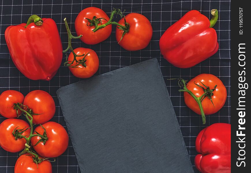 Red tomatoes on a branch, red pepper, cutting board slate on black cloth background with blank space for text. Flat lay. Top view