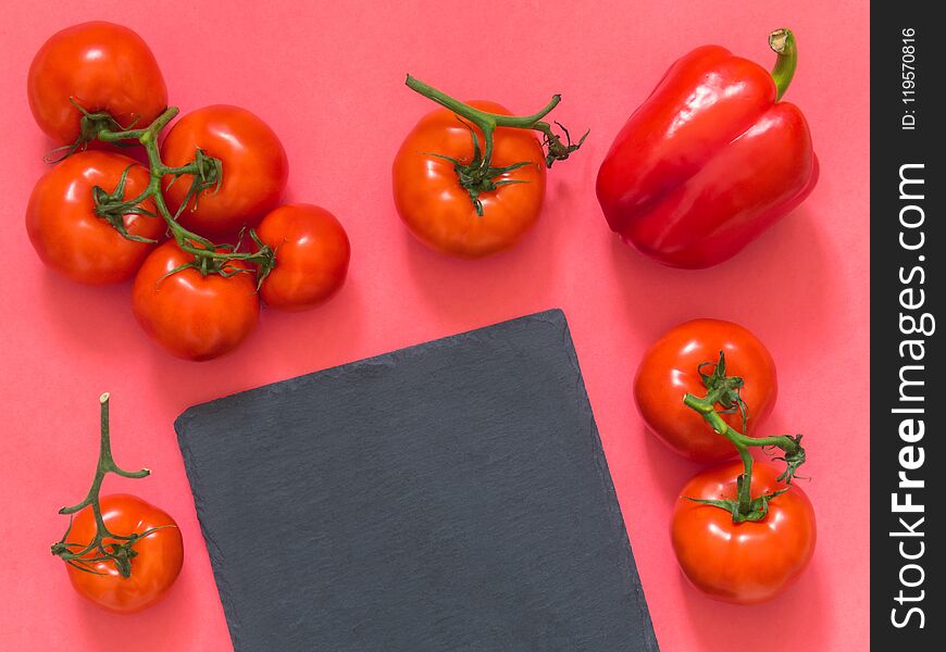 Red tomatoes on a branch, cutting board slate on a pink background with blank space for text. Flat lay. Top view. Copy space.