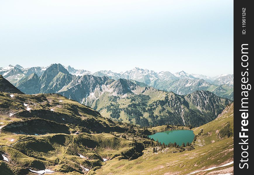 Beige and Green Mountain With Teal Lake Under White Sky at Daytime