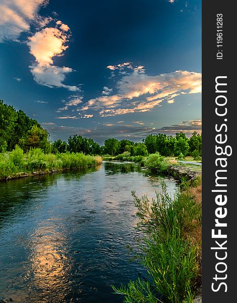 Body of Water and Green Field Under Blue Sky Photo