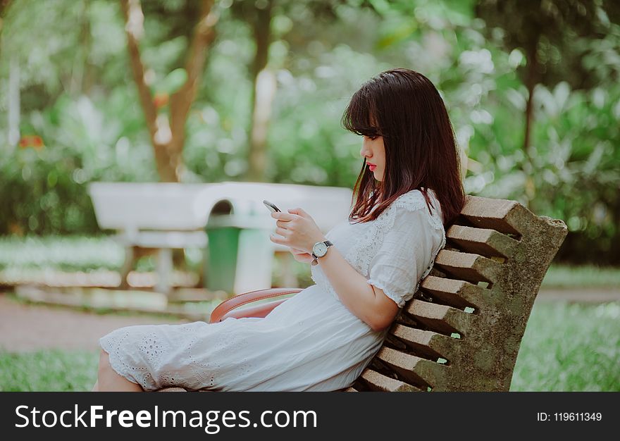Woman Sitting on Bench Checking Her Phone