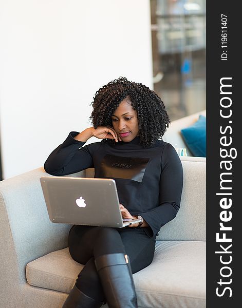 Woman in black outfit with MacBook sitting on a couch.