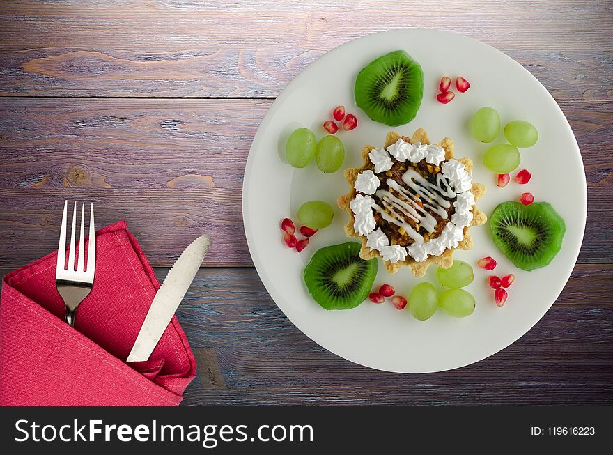 Dessert of cake and fruit grapes, kiwi, pomegranate on a wooden background. dessert on a plate top view