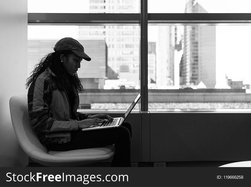 Grayscale Photo Of Woman Wearing Cap And Jacket Using Laptop