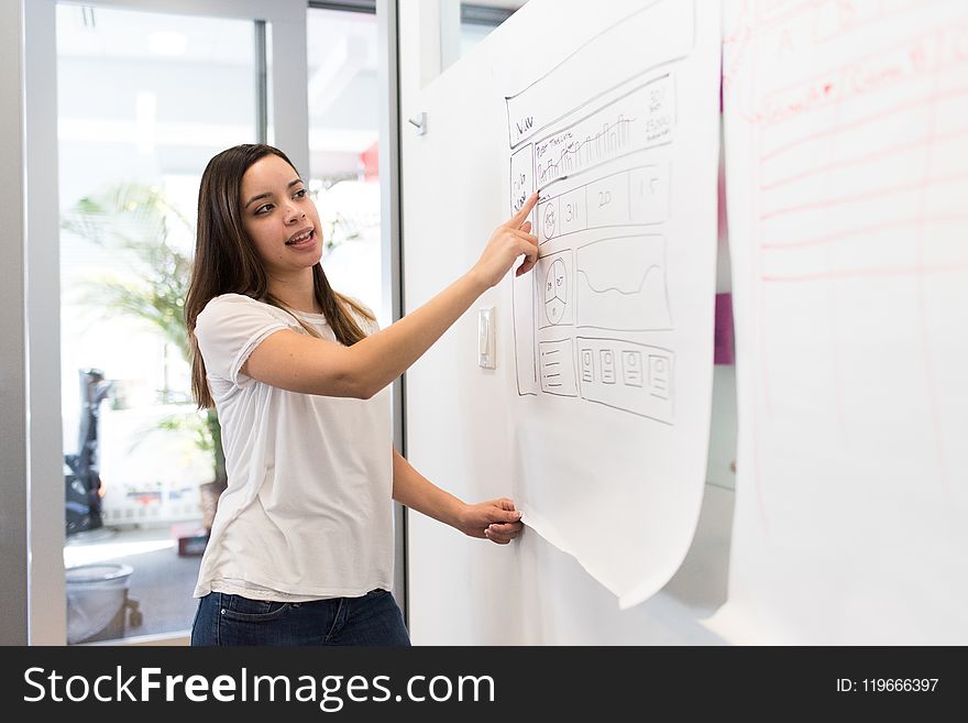 Woman Wearing White Shirt Standing Beside White Board While Pointing on White Paper