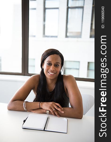 Woman Wearing Gray Tank Top and Sitting in Front of White Table With Spiral Notebook