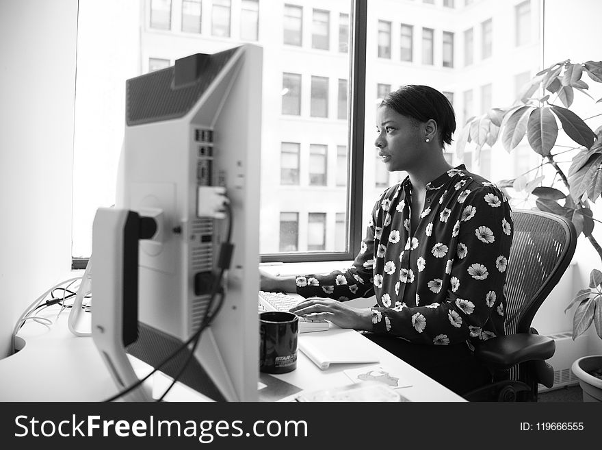 Gray Scale Photography of Woman Sitting on Armchair Facing Computer Monitor