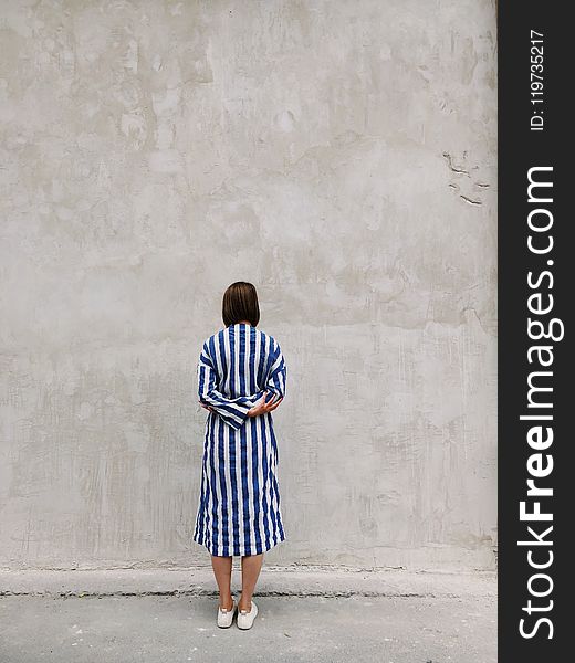 Woman Wearing Blue And White Striped Shirt Dress Facing Gray Wall